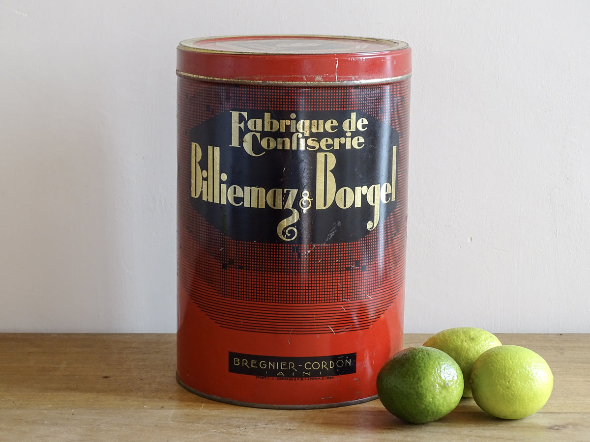 Vintage tin can with 'Fabrique de Confitèrie Billiémaz & Borge' branding on a wooden surface with limes.