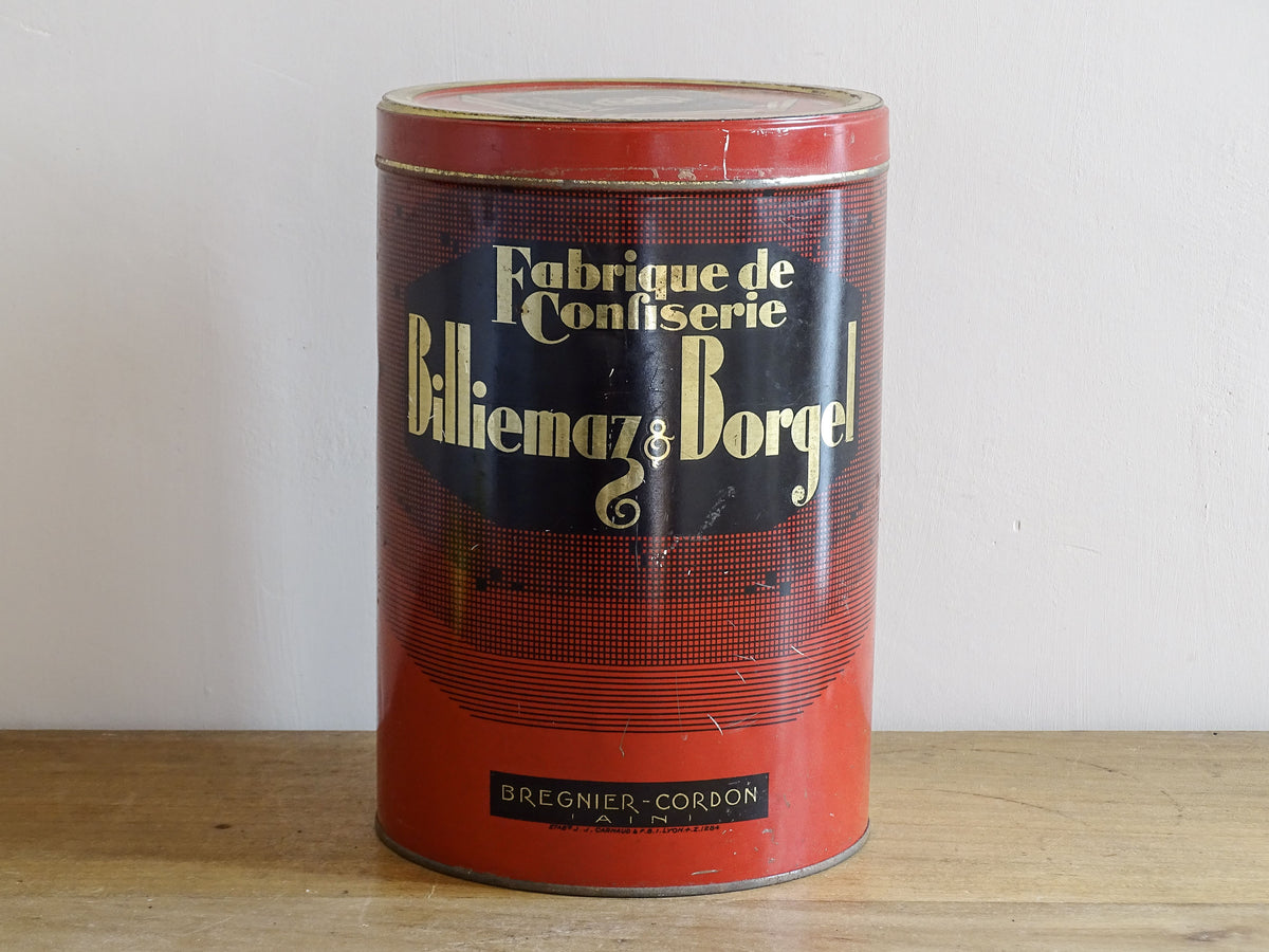 Vintage red and black canister with 'Fabrique de Confitèrie Billiemaiz & Borge' text on a wooden surface.
