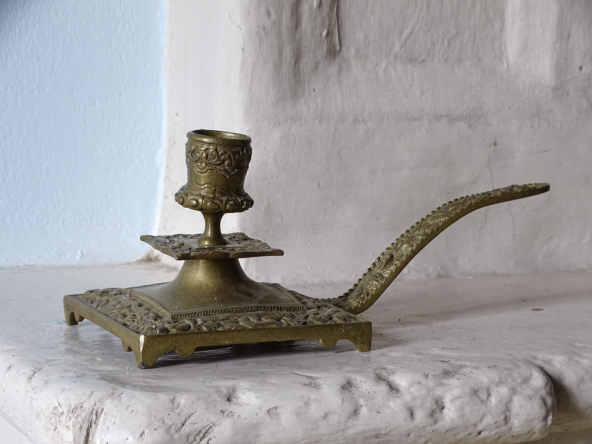 French antique brass candlestick holder with ornate detailing and handle, displayed on a country house fireplace