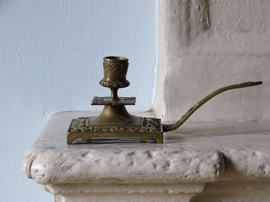 French antique brass candle holder, displayed on a country house fireplace next to a pale blue wall