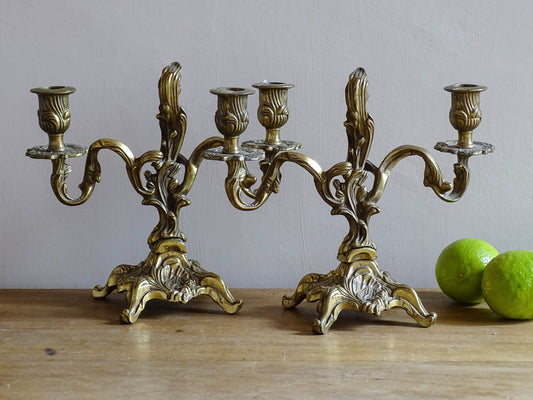 Pair of French antique brass candelabras in a rococo style. Early 20th century antique candelabras with space for two tapered candlesticks. Brass candle holders for dining table decor or living room decor.