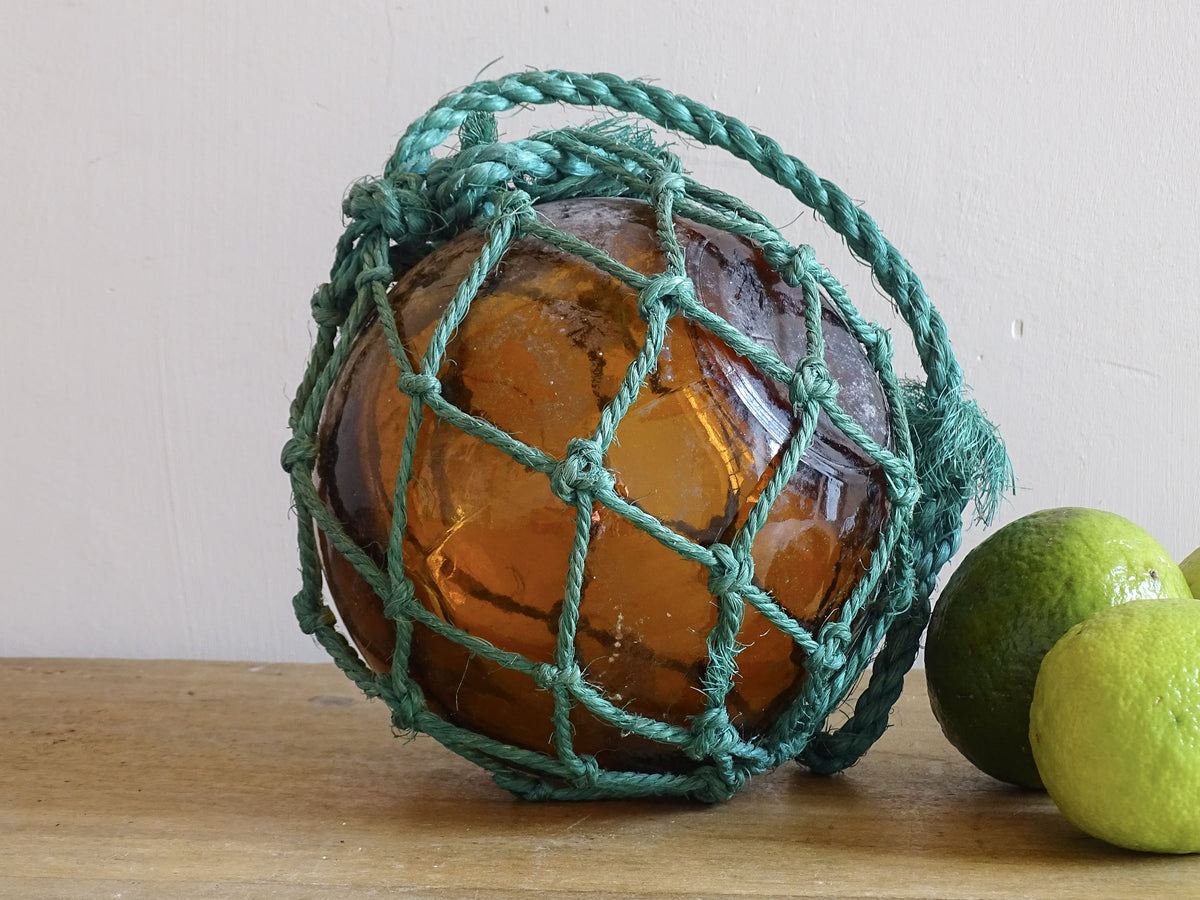 Amber glass ball in a green rope net on a wooden surface with limes in the background.