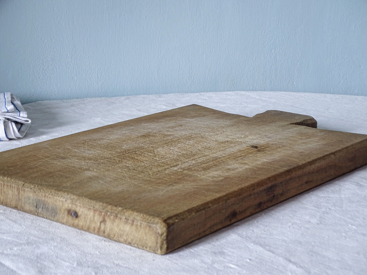 Angled side view of vintage French wooden cutting board showing its substantial thickness, warm wood grain and worn edges.