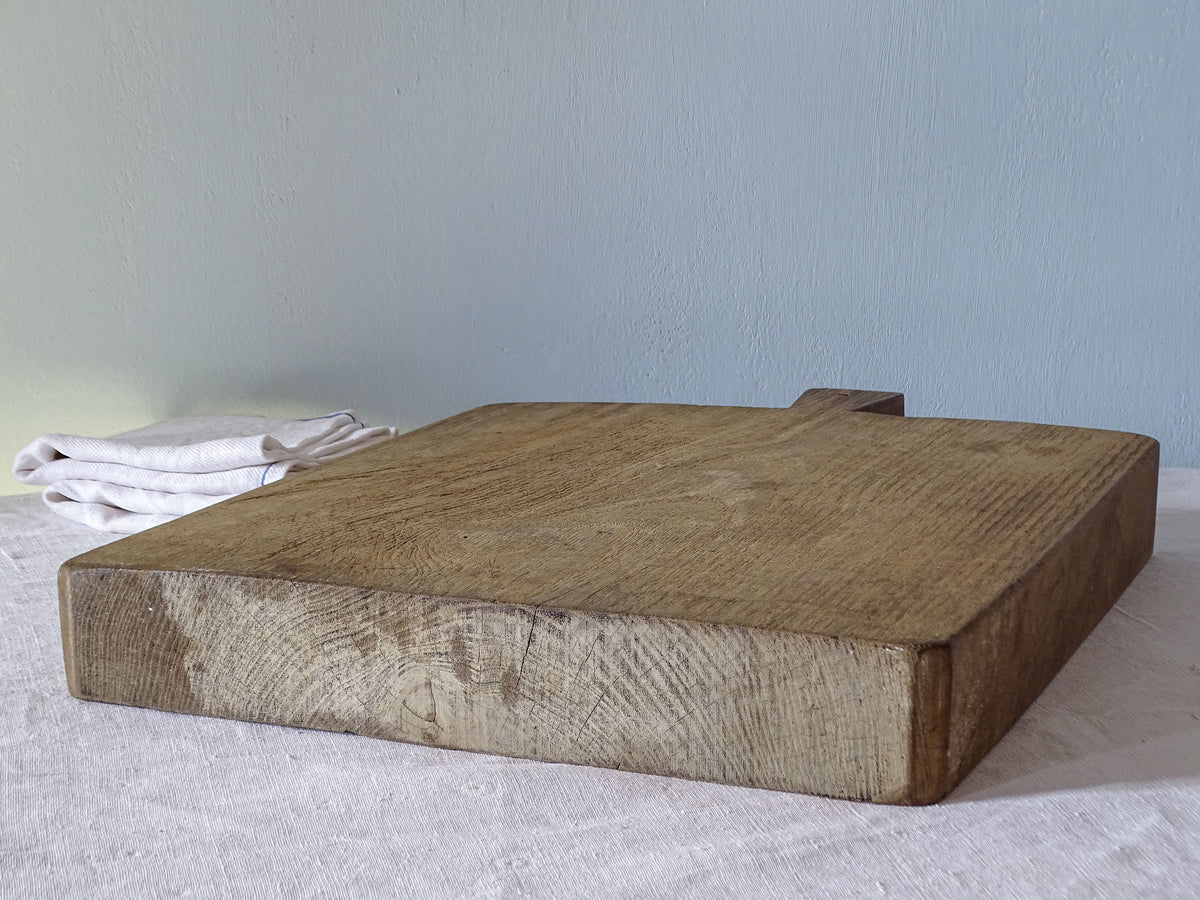 Angled view of large antique French wooden chopping board showing its substantial thickness, visible end grain and naturally worn surface.