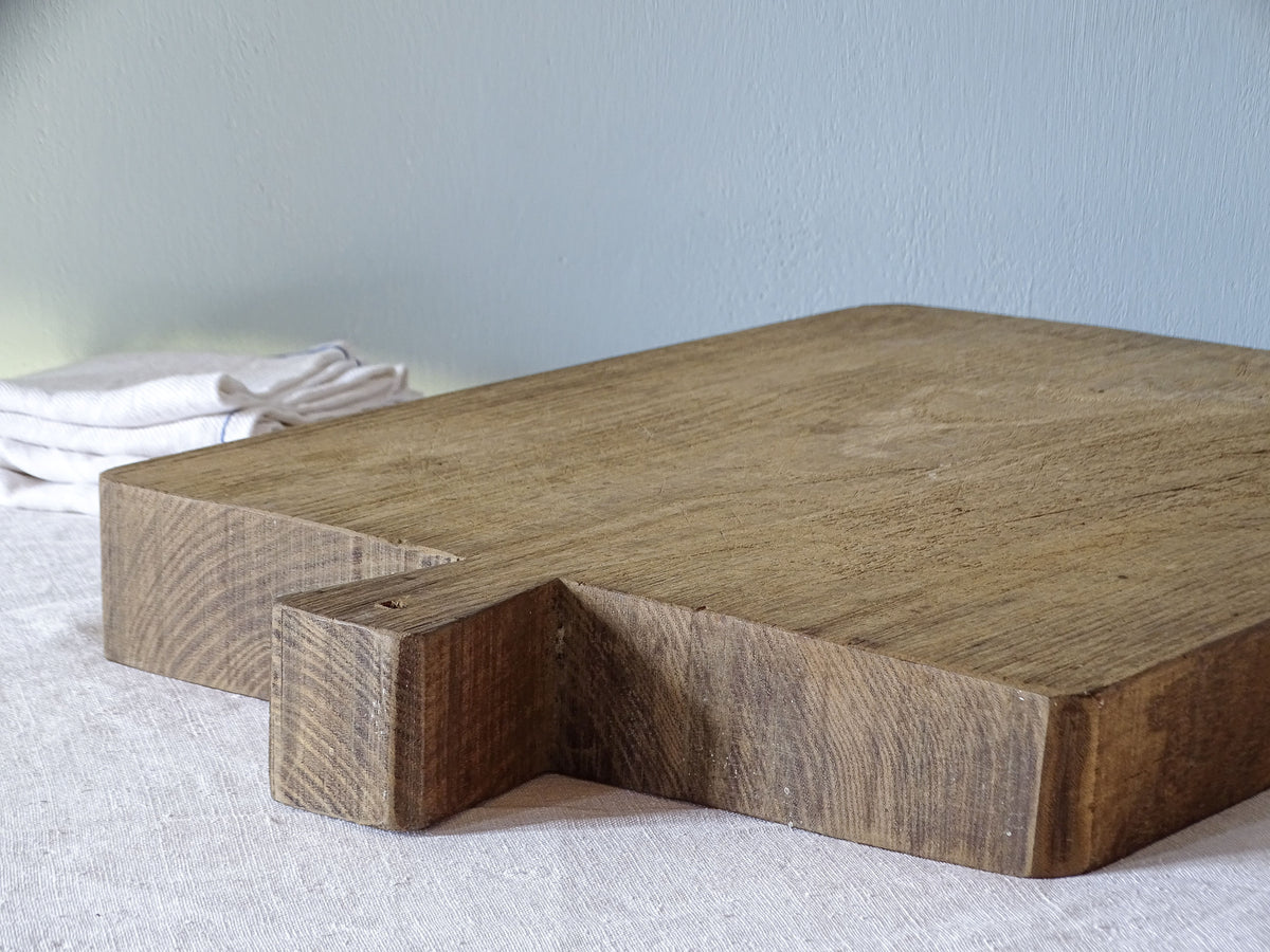 Close-up of antique French wooden cutting board showing the short integral handle, thick solid wood construction and natural grain.