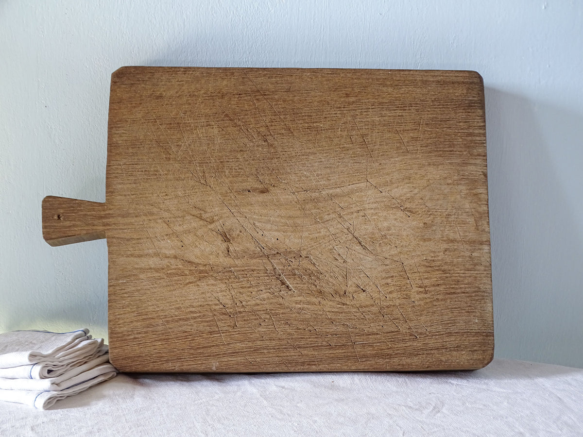 Antique French rectangular wooden cutting board with short integral handle, rounded corners and beautifully worn cutting surface.