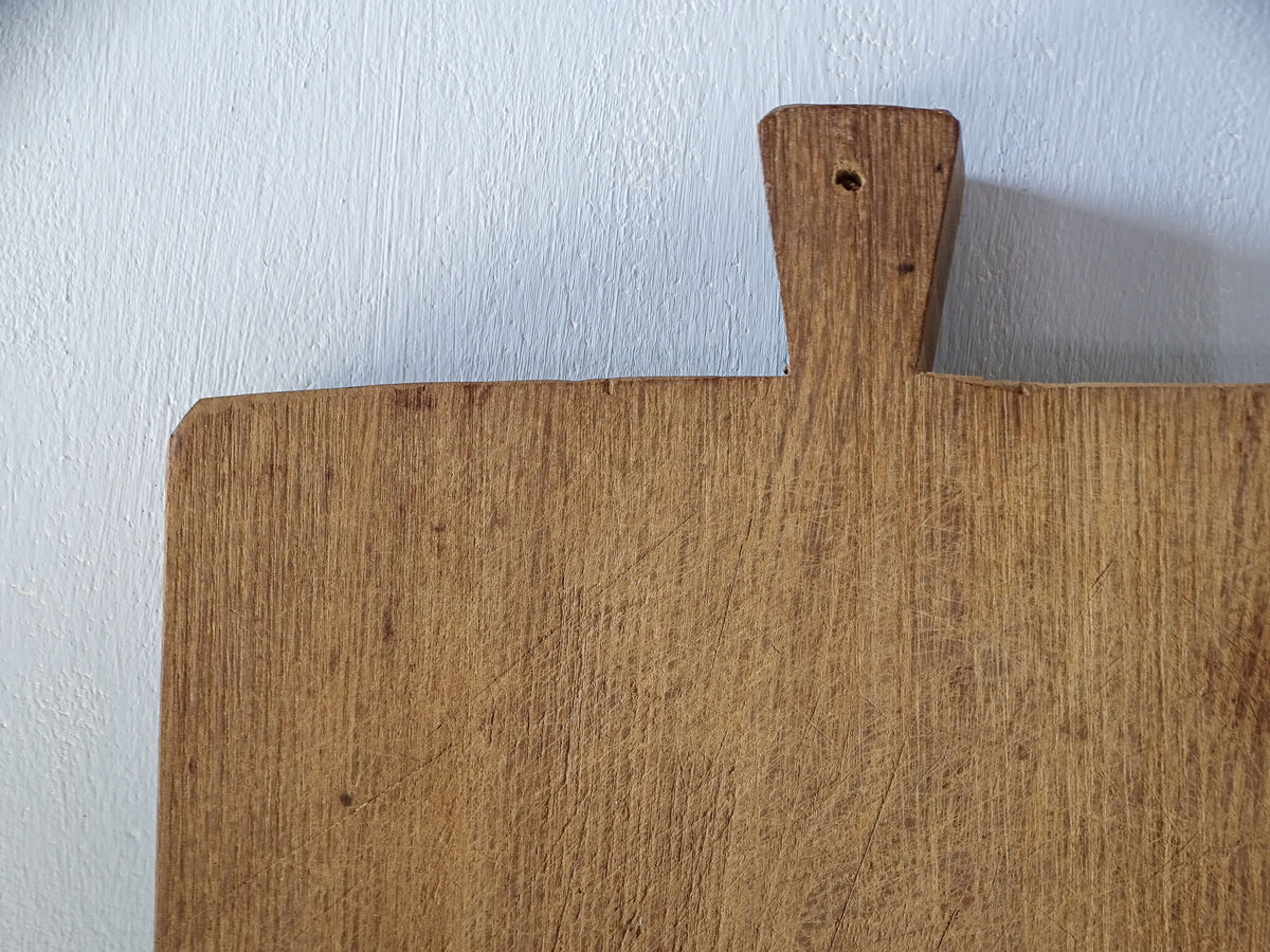 Detail of integral wooden handle with hanging hole on a substantial antique French chopping board, showing warm wood grain and surface wear.