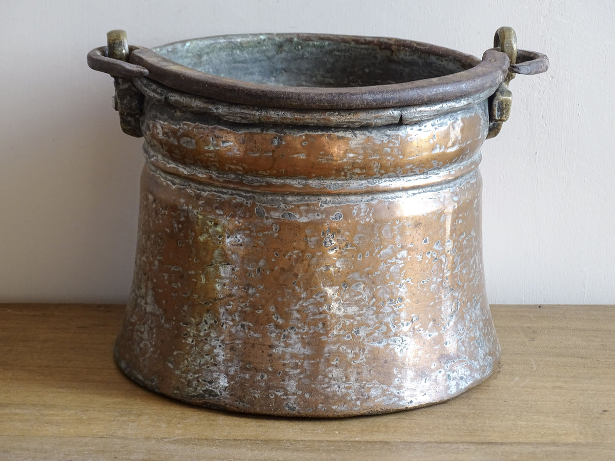 French antique tinned copper cauldron with brass detailing. A small antique copper cauldron with patina. A planter or utensil holder in a French country farmhouse kitchen.