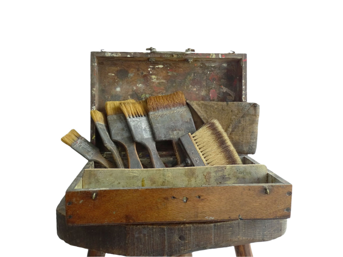 French antique paint box filled with paint brushes and painter’s tools. It has specks of paint and the outside of the wooden box has a “D” initial. The artist's box or painter's box has a rich patina.