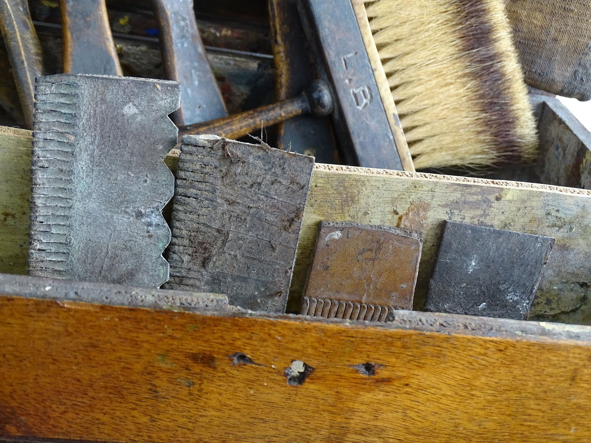 French antique paint box filled with paint brushes and painter’s tools. It has specks of paint and the outside of the wooden box has a “D” initial. The artist's box or painter's box has a rich patina.