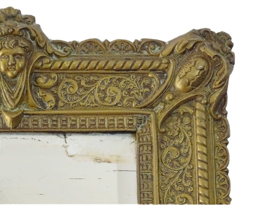 Small French antique brass mirror. The frame is embossed and decorated with a face, flowers and scroll design. Antique French mirror or Foxed mirror.