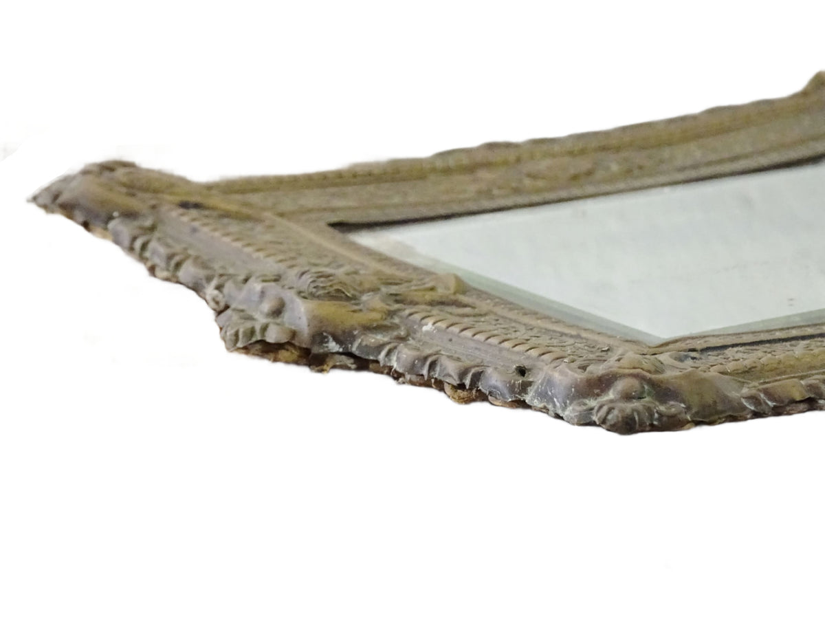 Small French antique brass mirror. The frame is embossed and decorated with a face, flowers and scroll design. Antique French mirror or Foxed mirror.