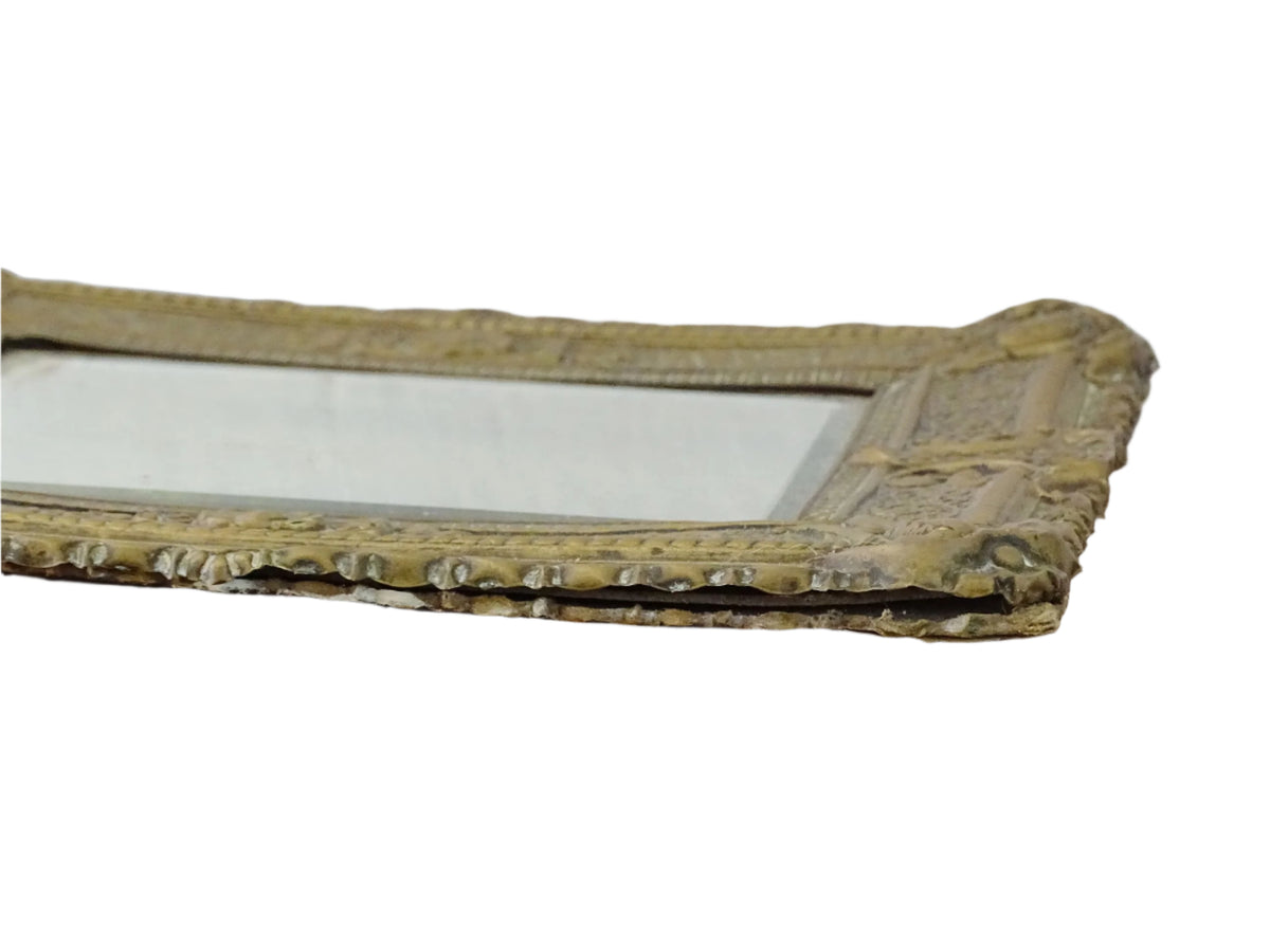 Small French antique brass mirror. The frame is embossed and decorated with a face, flowers and scroll design. Antique French mirror or Foxed mirror.
