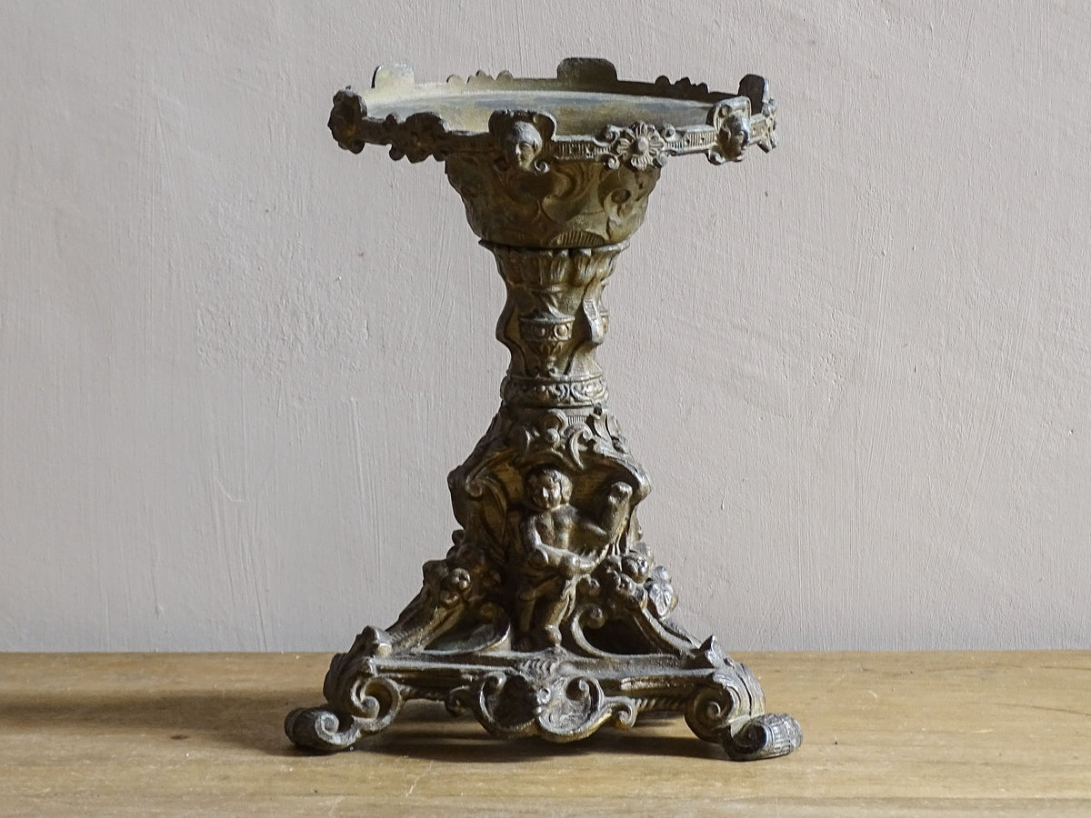 Ornate French antique cast iron candle holder with tripod base and decorated with cherubs.