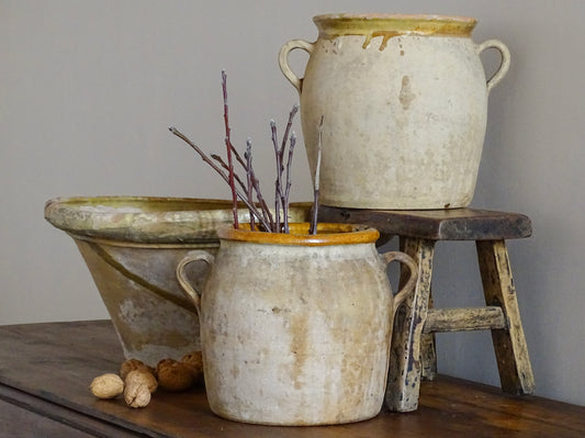 French antique cache pots or confit jars with yellow glaze interior, alongside a large antique tian bowl with yellow glaze. All sitting on a patinated wooden table.