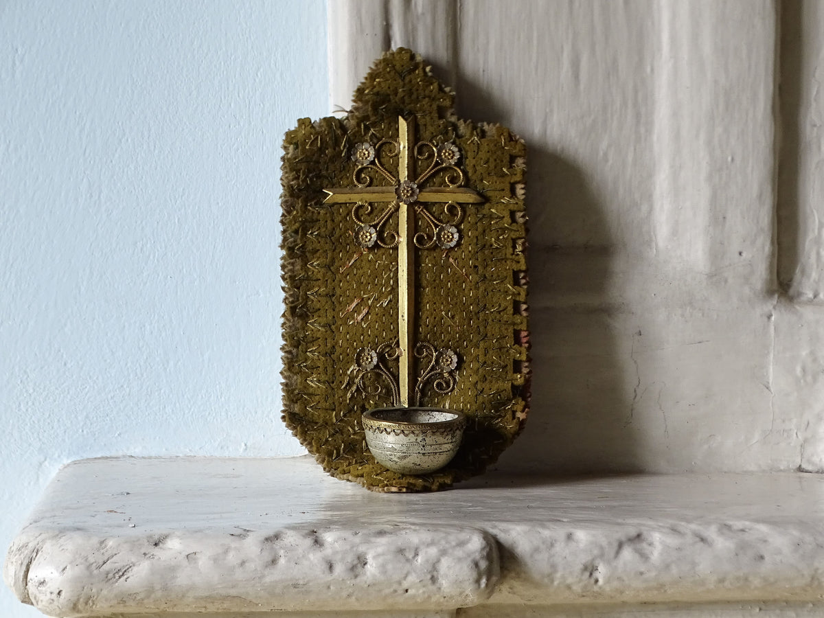 French antique holy water font with floral decorated cross on fabric, pictured on a country house fireplace mantel