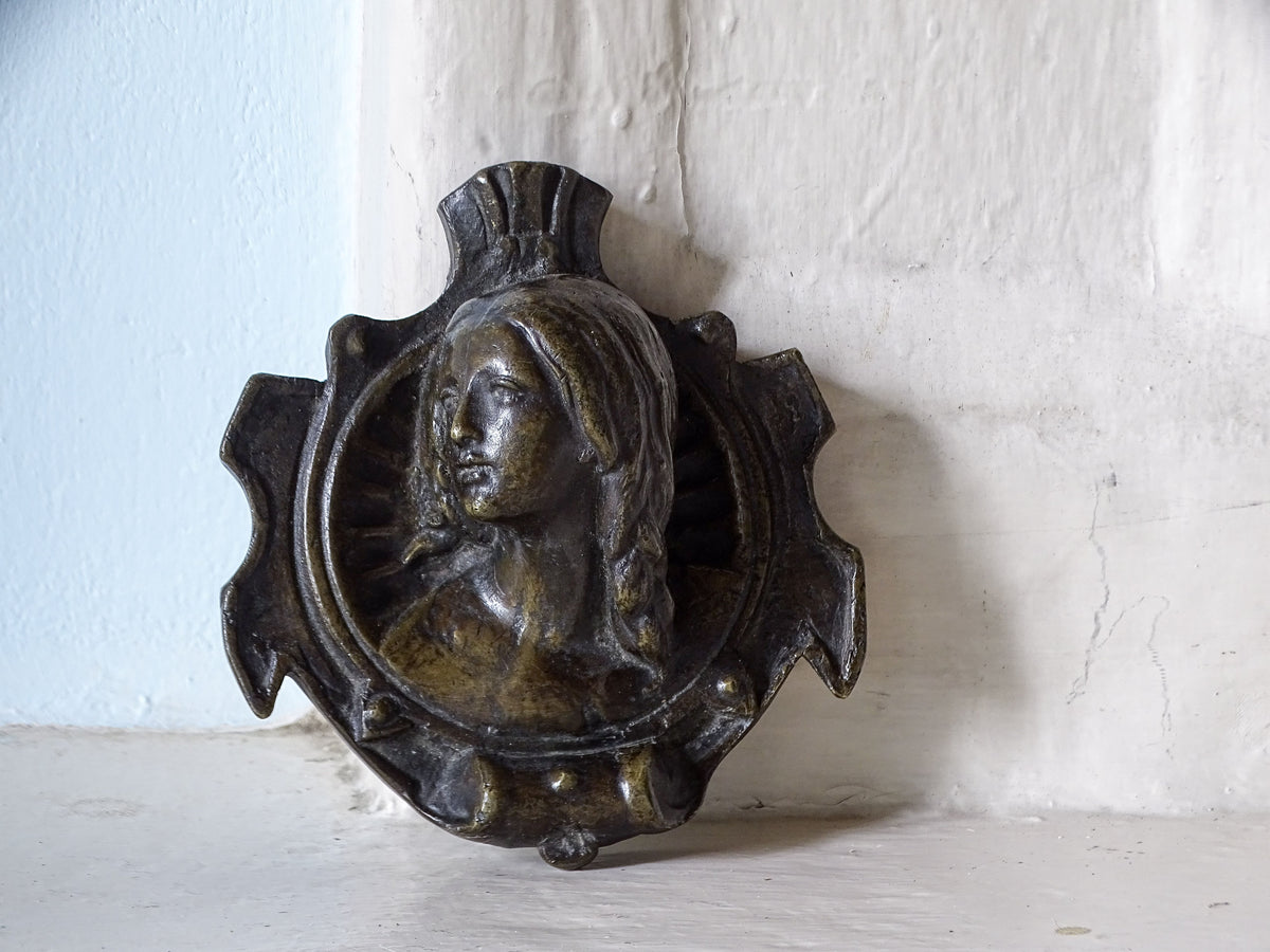 French antique bronze plaque featuring a relief bust of a woman's face, displayed on a country house fireplace.