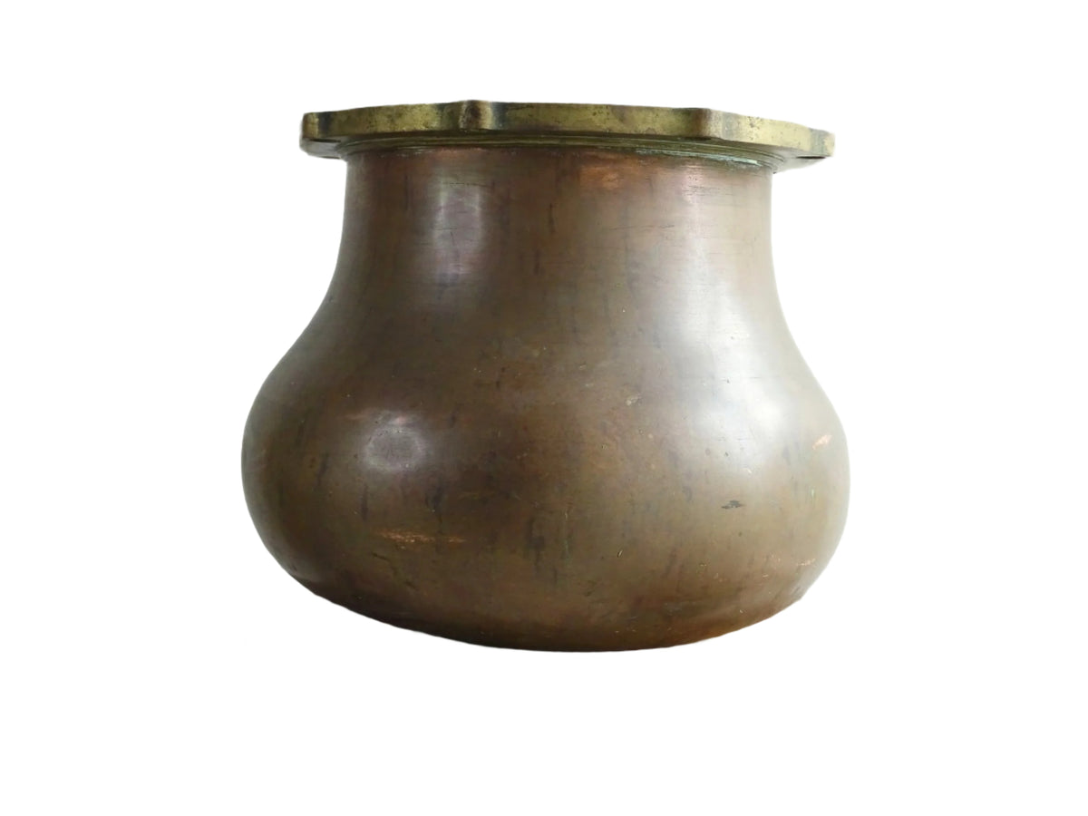 A large antique copper cauldron with a thick brass rim featuring evenly spaced holes, displayed on a rustic wooden surface. The cauldron has a weathered patina, showcasing its aged character.