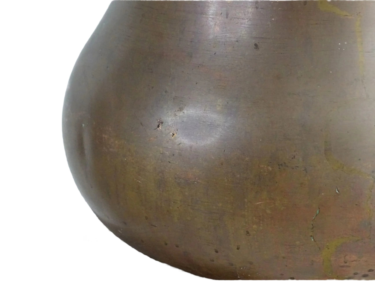 A large antique copper cauldron with a thick brass rim featuring evenly spaced holes, displayed on a rustic wooden surface. The cauldron has a weathered patina, showcasing its aged character.