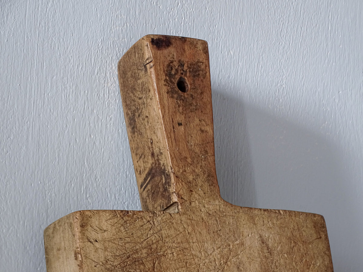 Close-up of antique French wooden cutting board handle with hanging hole, worn edges and dark aged patina.