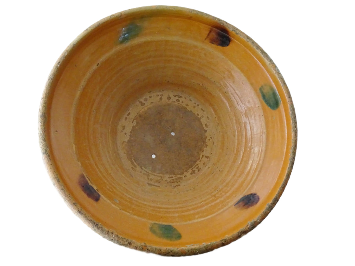 Large French antique pottery bowl with an orange glaze and blushes of green and blue. Timeworn terracotta bowl or basin has two holes in the bottom. Pottery colander or pottery strainer.