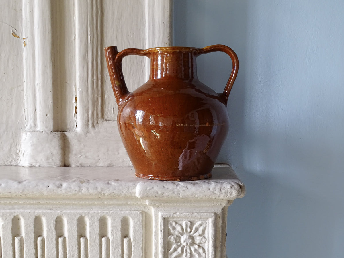 Large French antique ceramic pitcher or orjol with a red glaze on an old country fireplace