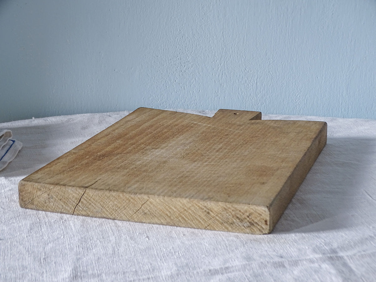 Angled view of vintage French wooden cutting board showing its thickness, worn surface and small age-related cracks along the edge.