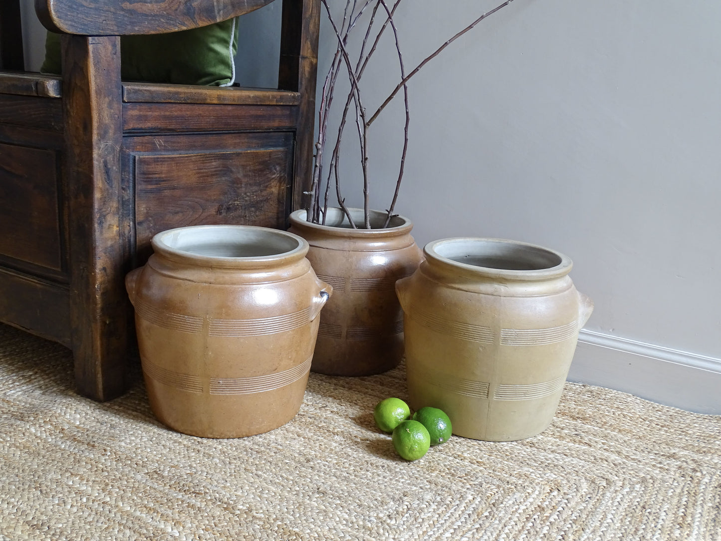 Three ceramic pots on a jute rug with a wooden chair and limes