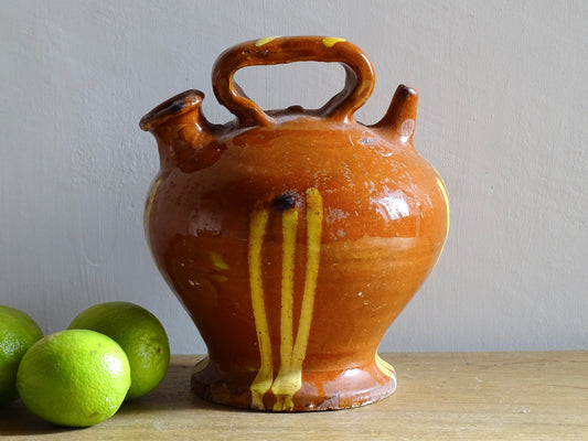 Rustic French antique pottery cruche or gargoulette with a red brown glaze and yellow stripes. Antique terracotta pitcher with a rounded shape with a handle to the top and two spouts. Provencal style farmhouse table decor.