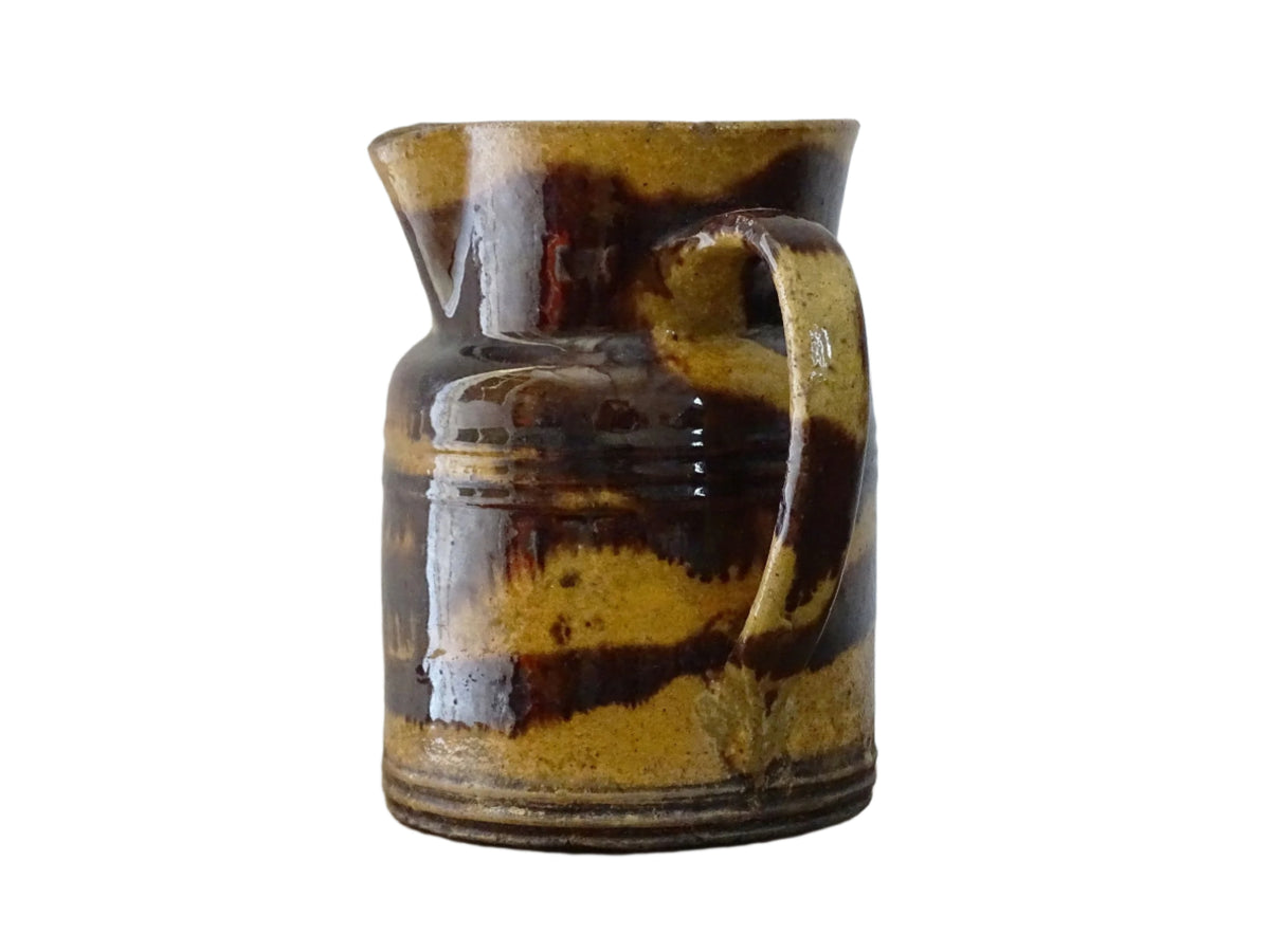 Rustic French antique ceramic jug with a brown drip glaze on a deep mustard colour background. Pottery jug from Dieulefit with a side spout. Rustic French pottery for a French farmhouse aesthetic.