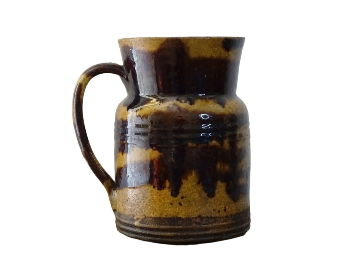 Rustic French antique ceramic jug with a brown drip glaze on a deep mustard colour background. Pottery jug from Dieulefit with a side spout. Rustic French pottery for a French farmhouse aesthetic.