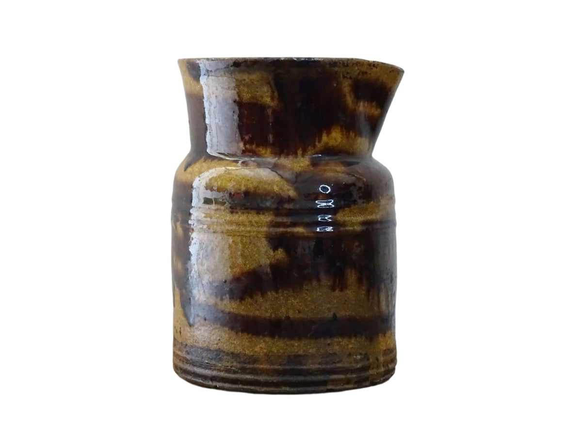 Rustic French antique ceramic jug with a brown drip glaze on a deep mustard colour background. Pottery jug from Dieulefit with a side spout. Rustic French pottery for a French farmhouse aesthetic.