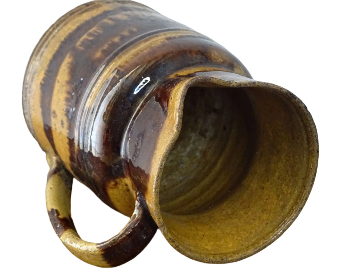 Rustic French antique ceramic jug with a brown drip glaze on a deep mustard colour background. Pottery jug from Dieulefit with a side spout. Rustic French pottery for a French farmhouse aesthetic.