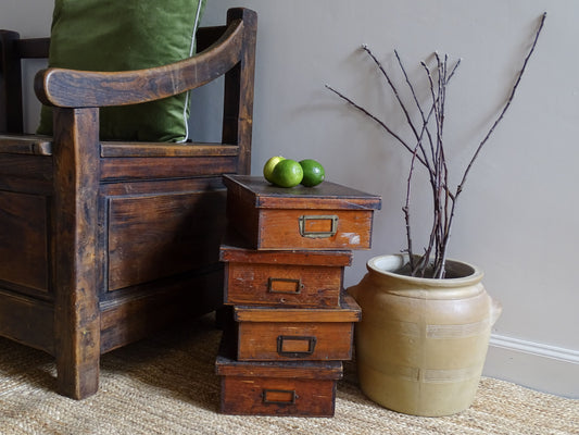 Set of four French antique wooden filing boxes next to a confit pot filled with branches. Both sit upon a natural jute rug, alongside an antique wooden seat.