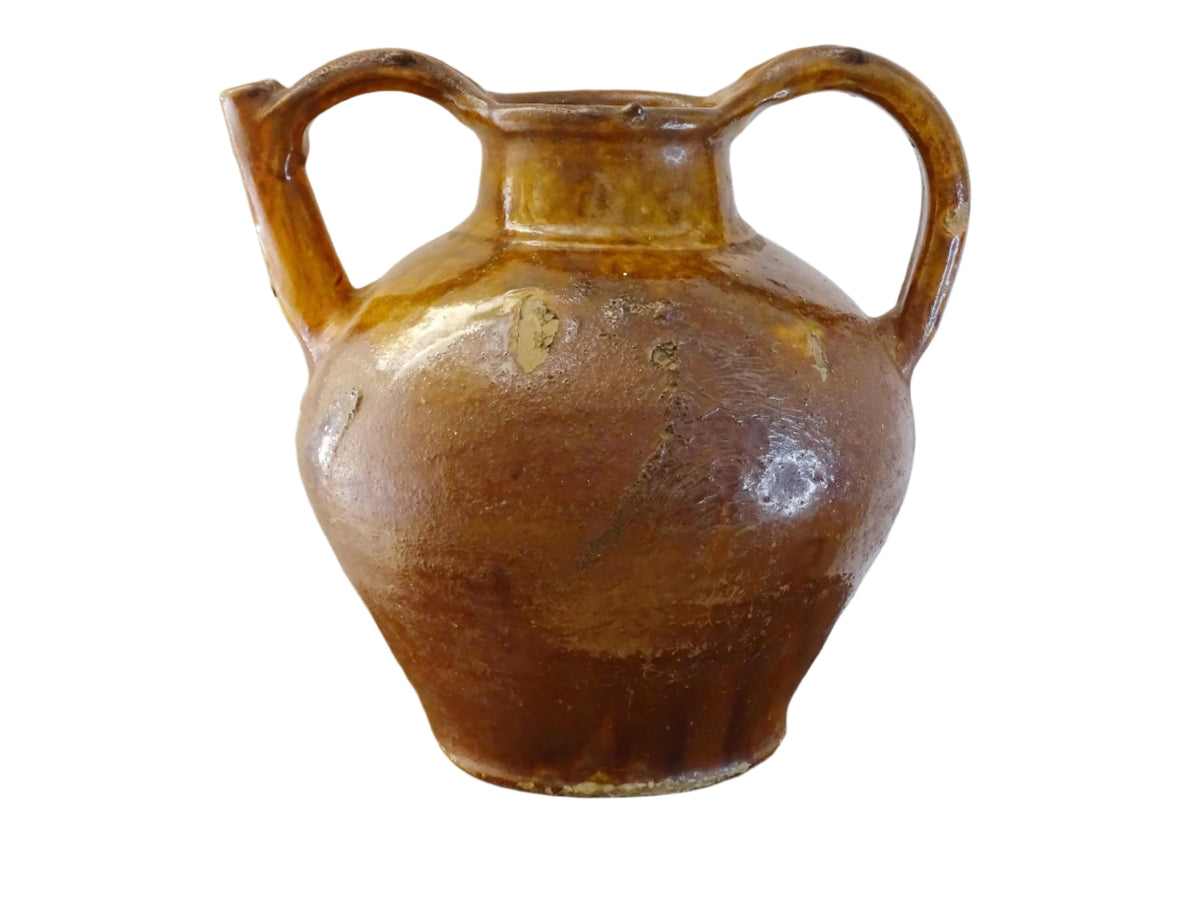 French antique pottery orjol or cruche with a golden caramel and yellow glaze. Glazed antique terracotta pitcher has two handles and a spout with a rounded body. Earthenware pottery for an antique French farmhouse style aesthetic.