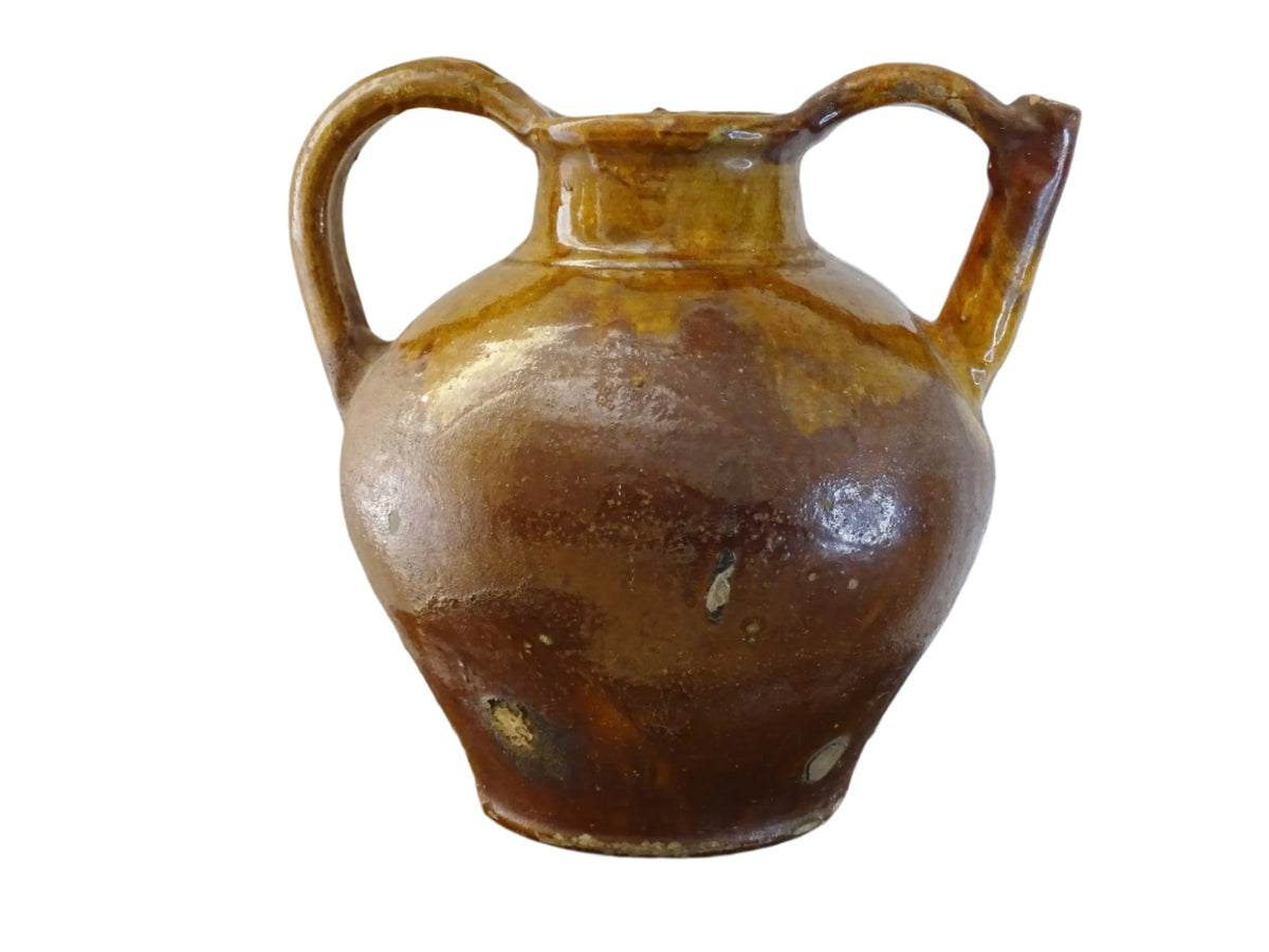 French antique pottery orjol or cruche with a golden caramel and yellow glaze. Glazed antique terracotta pitcher has two handles and a spout with a rounded body. Earthenware pottery for an antique French farmhouse style aesthetic.