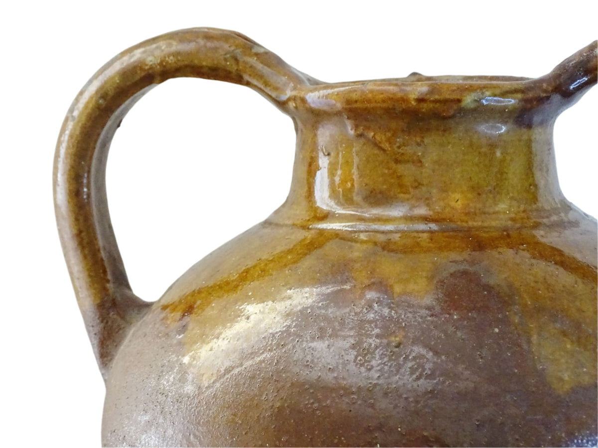 French antique pottery orjol or cruche with a golden caramel and yellow glaze. Glazed antique terracotta pitcher has two handles and a spout with a rounded body. Earthenware pottery for an antique French farmhouse style aesthetic.