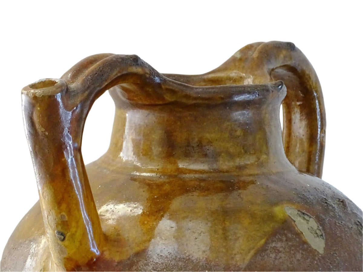French antique pottery orjol or cruche with a golden caramel and yellow glaze. Glazed antique terracotta pitcher has two handles and a spout with a rounded body. Earthenware pottery for an antique French farmhouse style aesthetic.