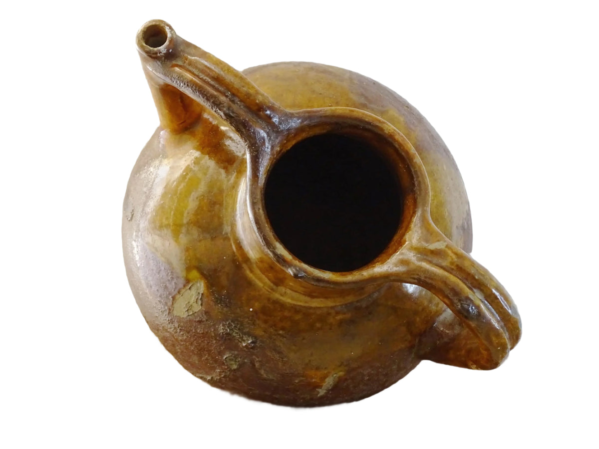 French antique pottery orjol or cruche with a golden caramel and yellow glaze. Glazed antique terracotta pitcher has two handles and a spout with a rounded body. Earthenware pottery for an antique French farmhouse style aesthetic.