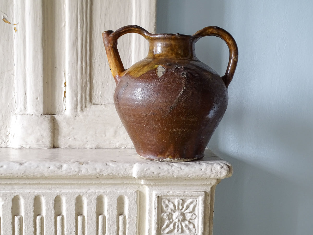 French antique ceramic pitcher or orjol with a golden caramel and yellow glaze, pictured on an old country house fireplace.
