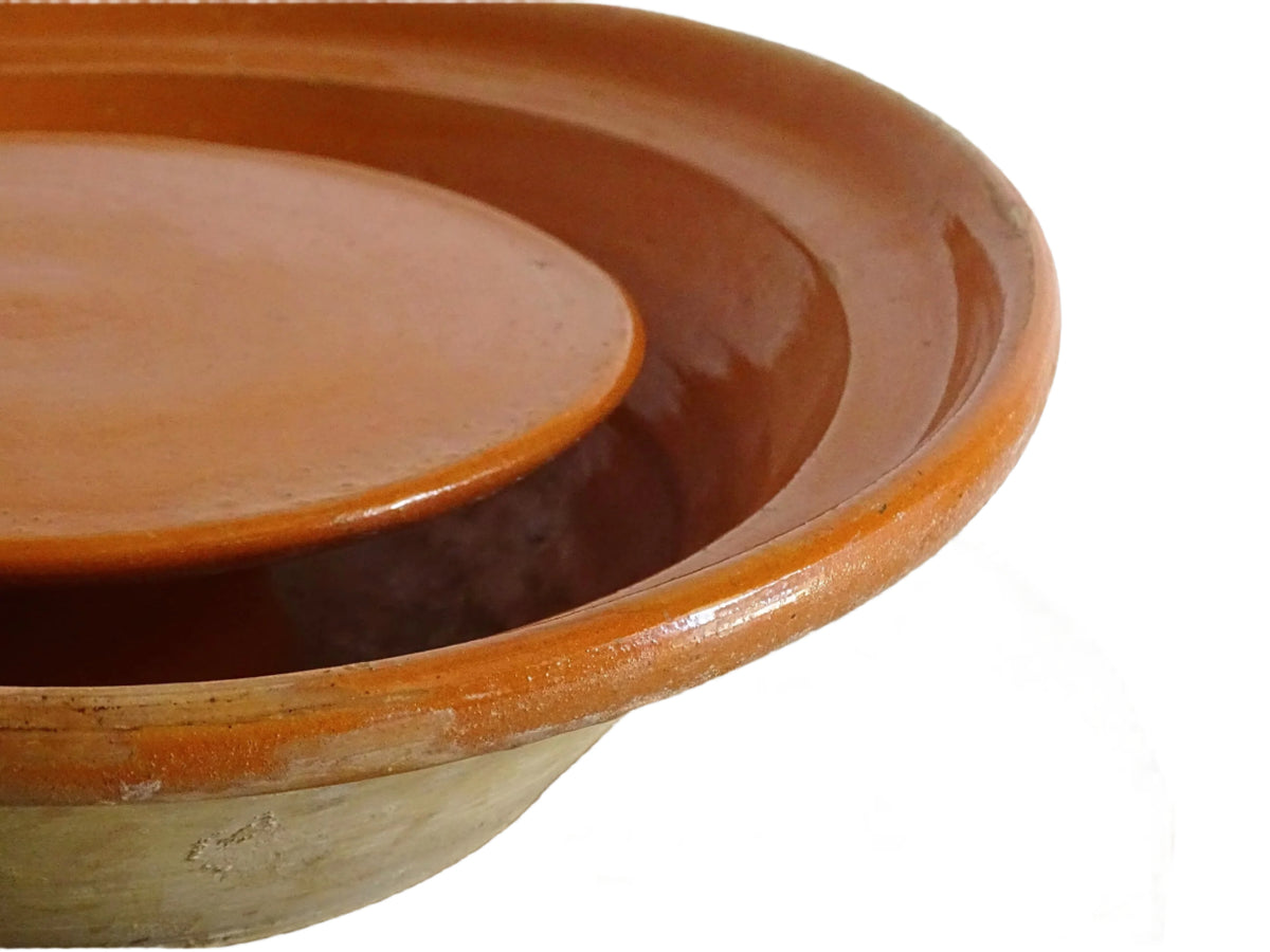 French antique pottery cheese strainer or faisseller. Shaped like a French tian bowl with a stand in the middle and a lip to the edge. Rustic French antique pottery bowl with an orange glaze. Glazed earthenware cheese drainer.