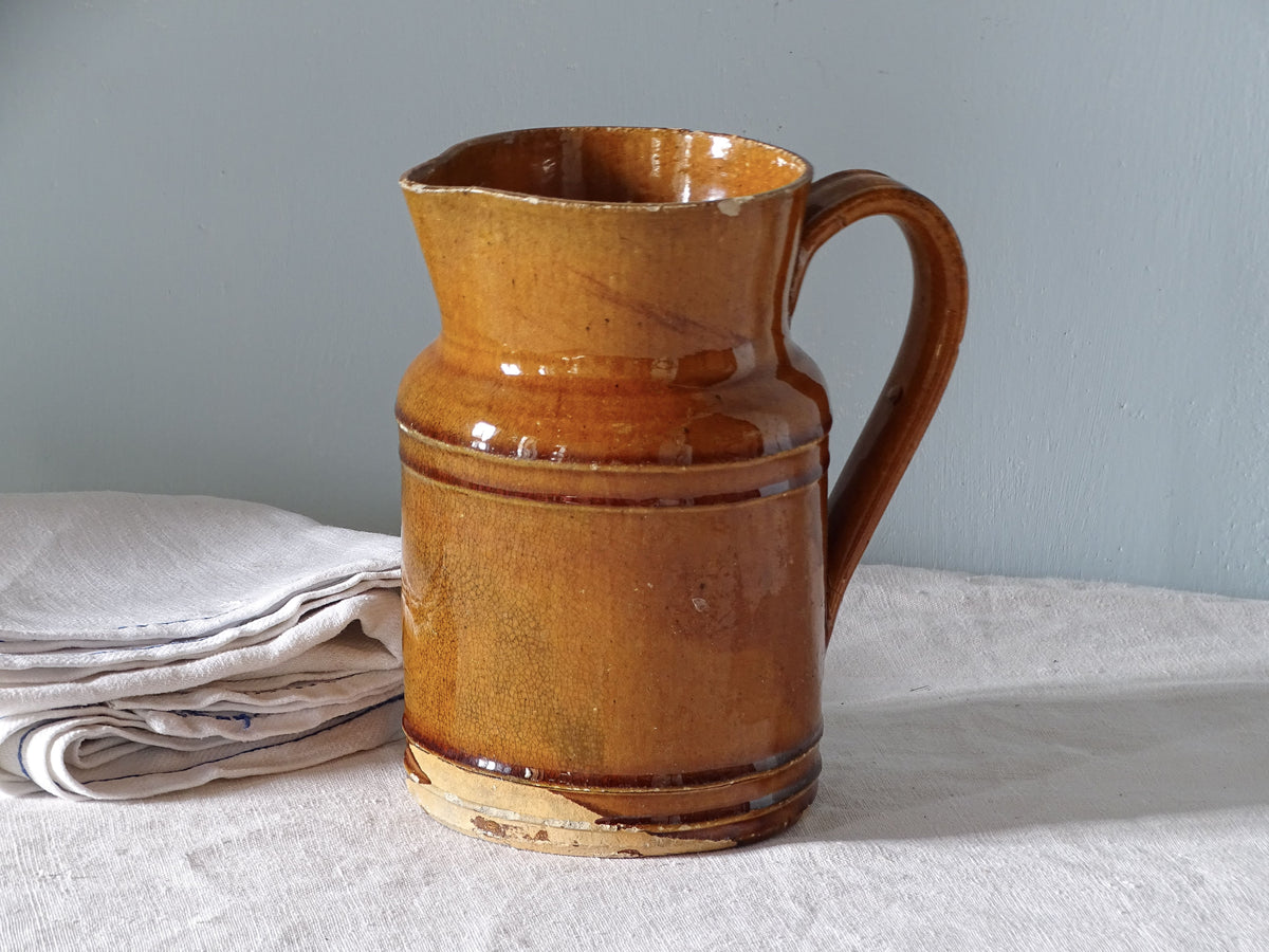 French antique ceramic jug with orange glaze, displayed with linen