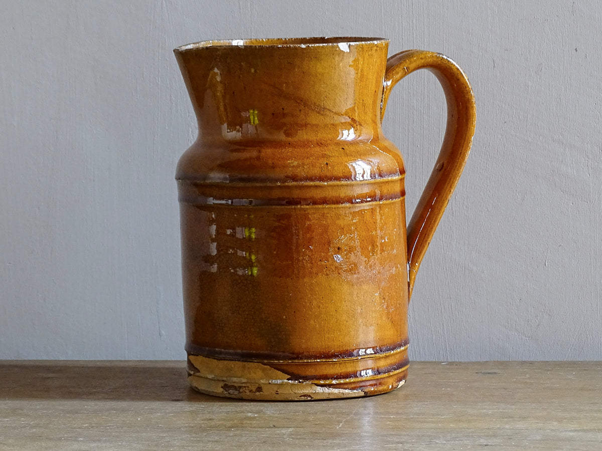 Rustic French antique pottery jug with an orange glaze. Glazed ceramic pitcher from Savoie. Savoyard pottery jug with a handle and spout.