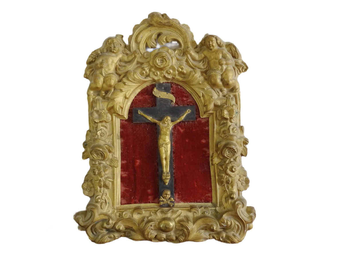 French antique crucifix in a gold frame on a red velvet background and Christ in gold. Gilt metal frame decorated with cherubs, roses and acanthus leaves in a rococo style. French antique religious decor.