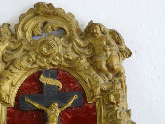 French antique crucifix in a gold frame on a red velvet background and Christ in gold. Gilt metal frame decorated with cherubs, roses and acanthus leaves in a rococo style. French antique religious decor.