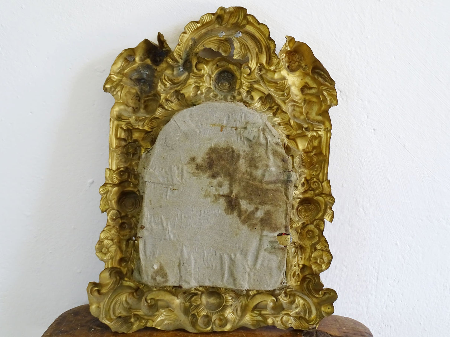 French antique crucifix in a gold frame on a red velvet background and Christ in gold. Gilt metal frame decorated with cherubs, roses and acanthus leaves in a rococo style. French antique religious decor.