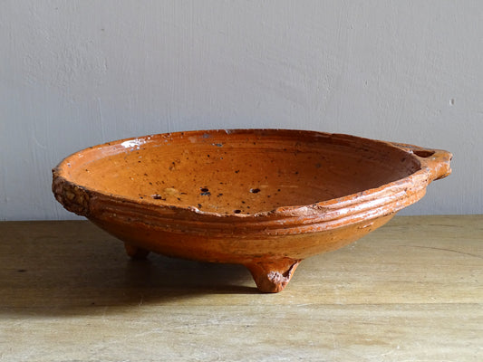 French antique terracotta sieve with orange glaze. Glazed pottery sieve on three pedestal feet. Rustic ceramic berry strainer for a farmhouse kitchen.