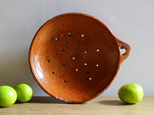 French antique terracotta sieve with orange glaze. Glazed pottery sieve on three pedestal feet. Rustic ceramic berry strainer for a farmhouse kitchen.