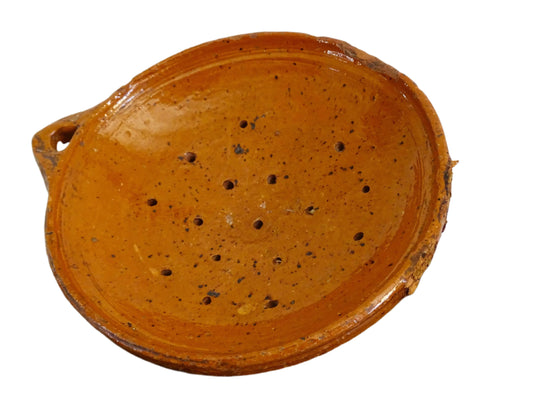 French antique terracotta sieve with orange glaze. Glazed pottery sieve on three pedestal feet. Rustic ceramic berry strainer for a farmhouse kitchen.