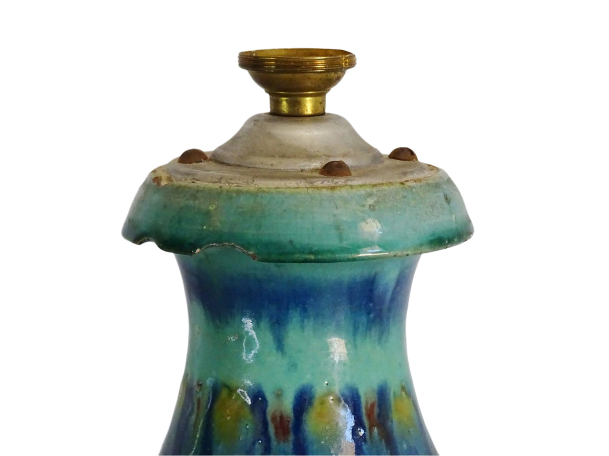 A French vintage ceramic vase lamp base with a bold, multicolored glaze in deep blue, green, and yellow. The organic, dripping pattern covers the surface, giving it a fluid, textured look. The vase has a rounded body that tapers towards a narrower neck, fitted with a brass lamp attachment. It rests on a slightly elevated base.